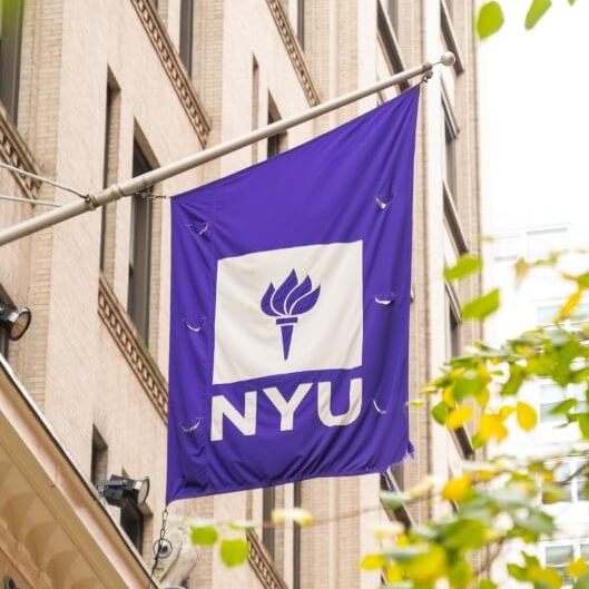 A purple-and-white NYU banner on the exterior of a building